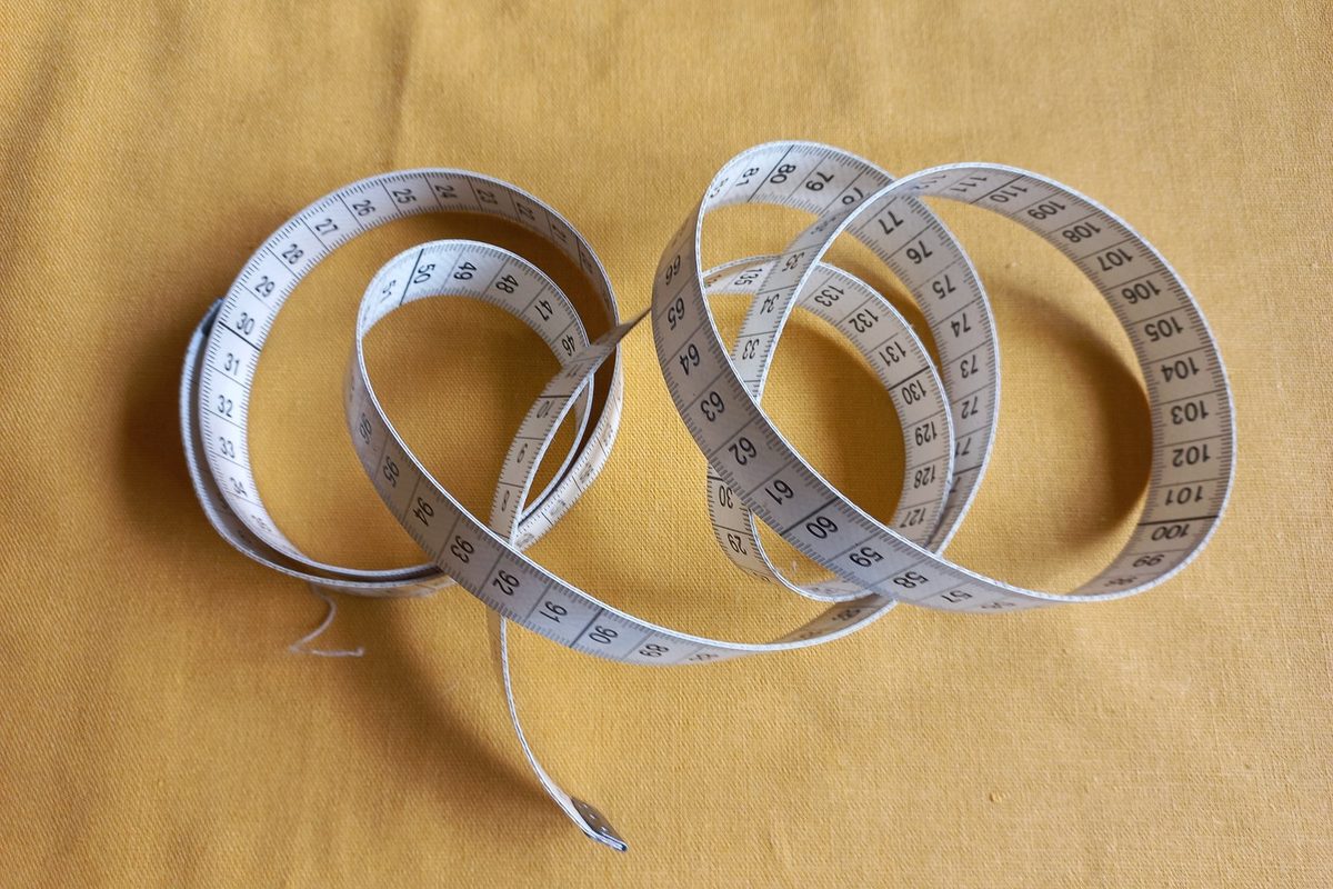 Cloth tape measure coiled on yellow fabric, the tool a homeowner uses to check the real square footage of a house