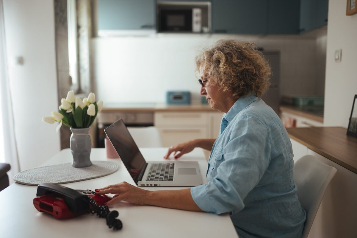 Laptop showing an online home value estimate next to a printed sheet of comparable sales, the check behind any estimator