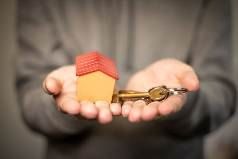Schlüsselübergabe vor einem Einfamilienhaus nach dem Verkauf, Sinnbild für Verkaufskosten und Nettoerlös