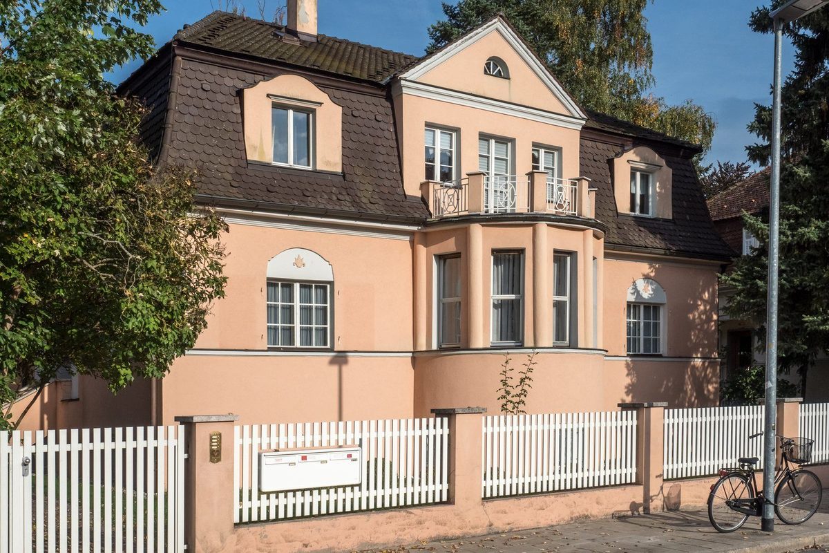Smartphone mit einer Immobilienbewertung in der Hand, im Hintergrund die Fassade eines Einfamilienhauses mit Garten