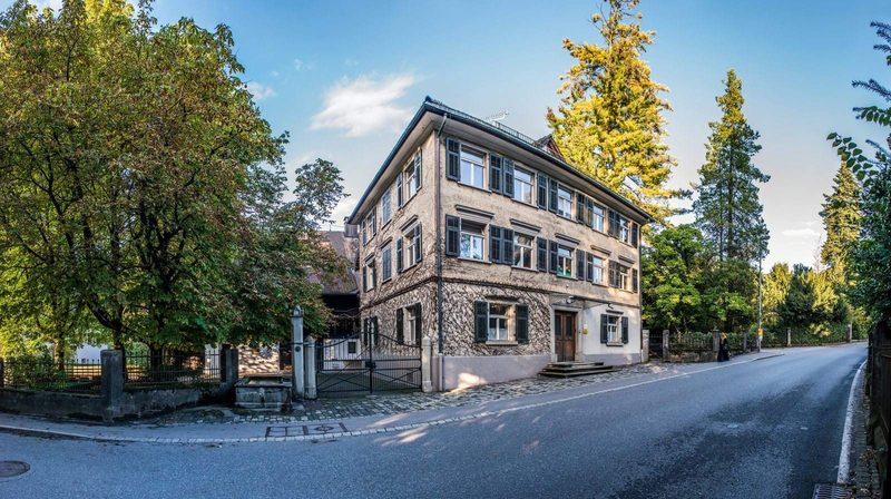 Gepflasterter Gehsteig mit Randstein vor einem Einfamilienhaus mit Gartenzaun und Hecke in einer österreichischen Wohnstraße