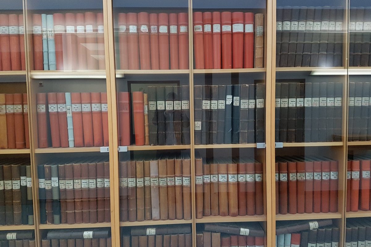 Aufgeschlagenes historisches Grundbuch mit handschriftlichen Eintragungen auf einem Holztisch in einem Gerichtsarchiv