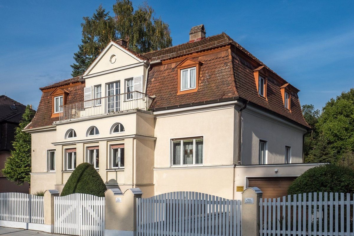 Einfamilienhaus mit Garten hinter einem Holzzaun, im Vordergrund ein Grenzstein zwischen zwei Grundstücken