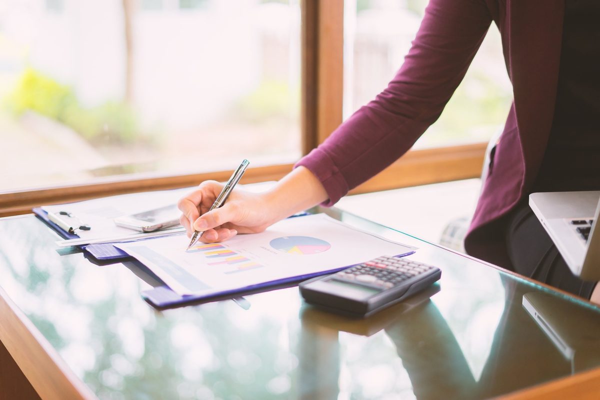Vermieterin am Schreibtisch mit Mietvertrag, Taschenrechner und einer Tabelle des Verbraucherpreisindex vor dem Schreiben eines Erhöhungsbegehrens
