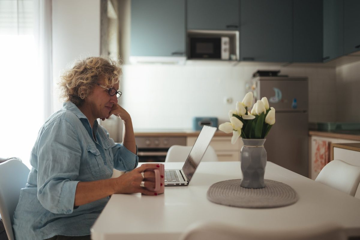 A homeowner reading a printed property tax bill at a kitchen table beside a laptop showing a county parcel search