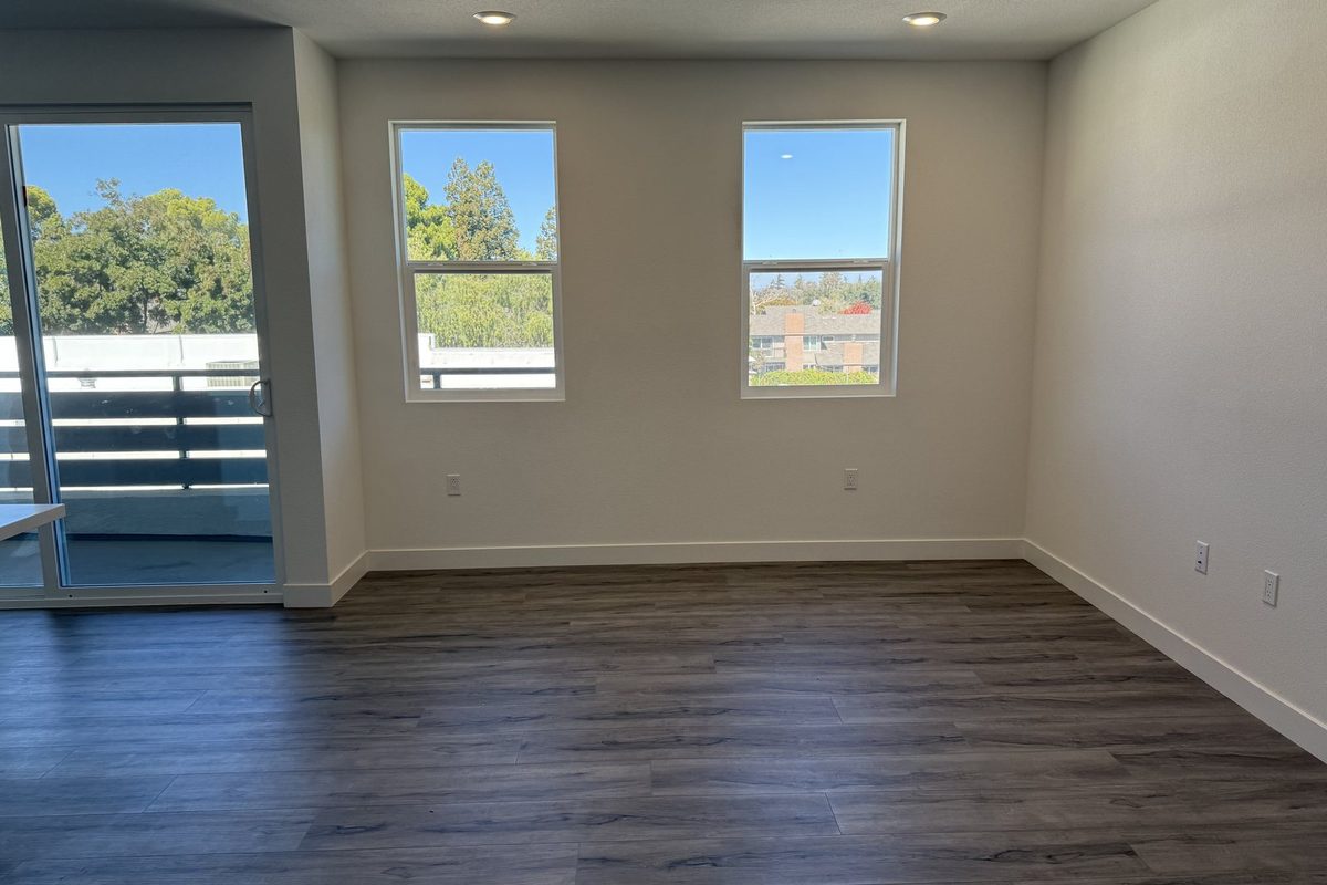 An empty living room with bare floorboards and tall windows, the view a buyer gets at a showing of a vacant house