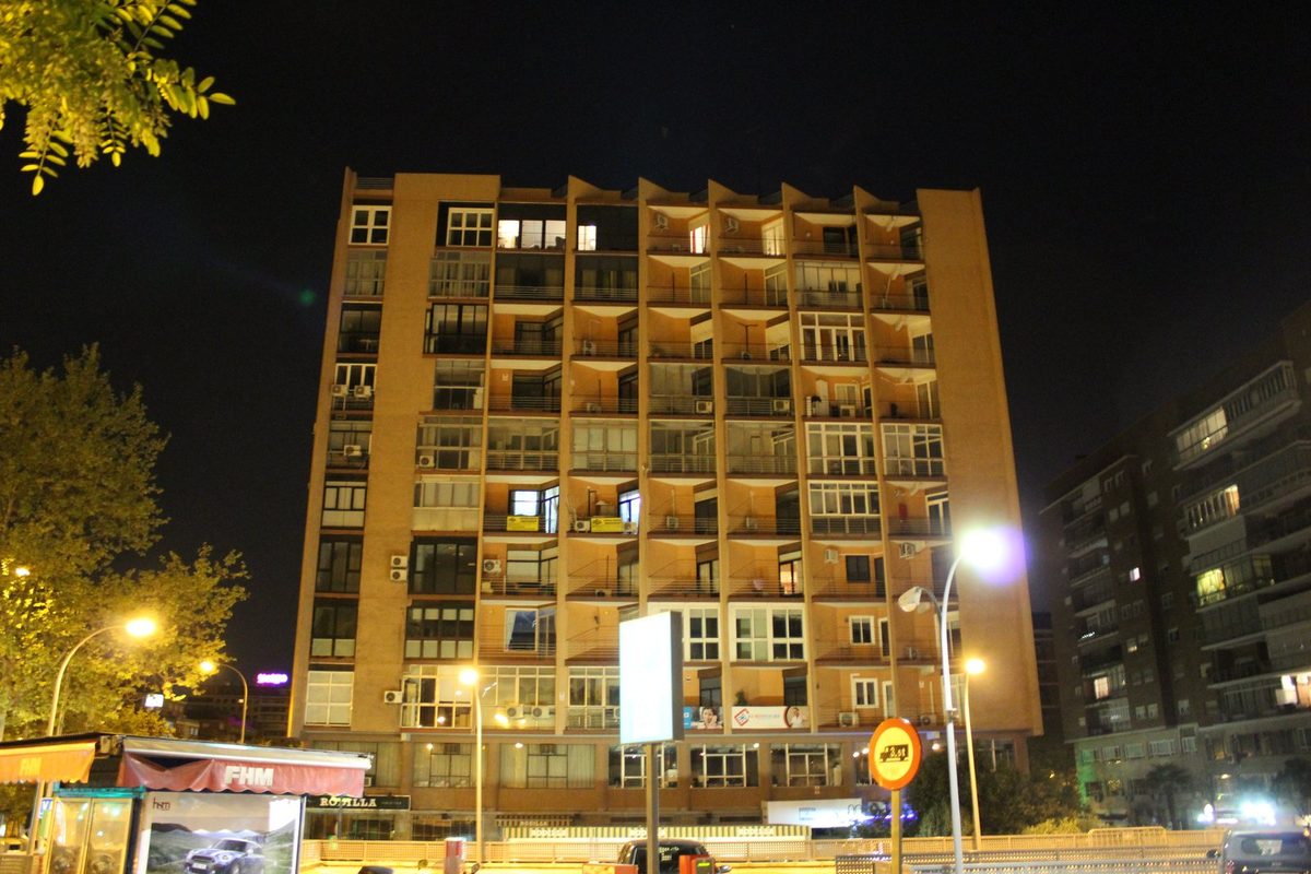 Edificio de viviendas de varias plantas en el paseo de la Castellana de Madrid, de noche, con balcones acristalados y ventanas iluminadas