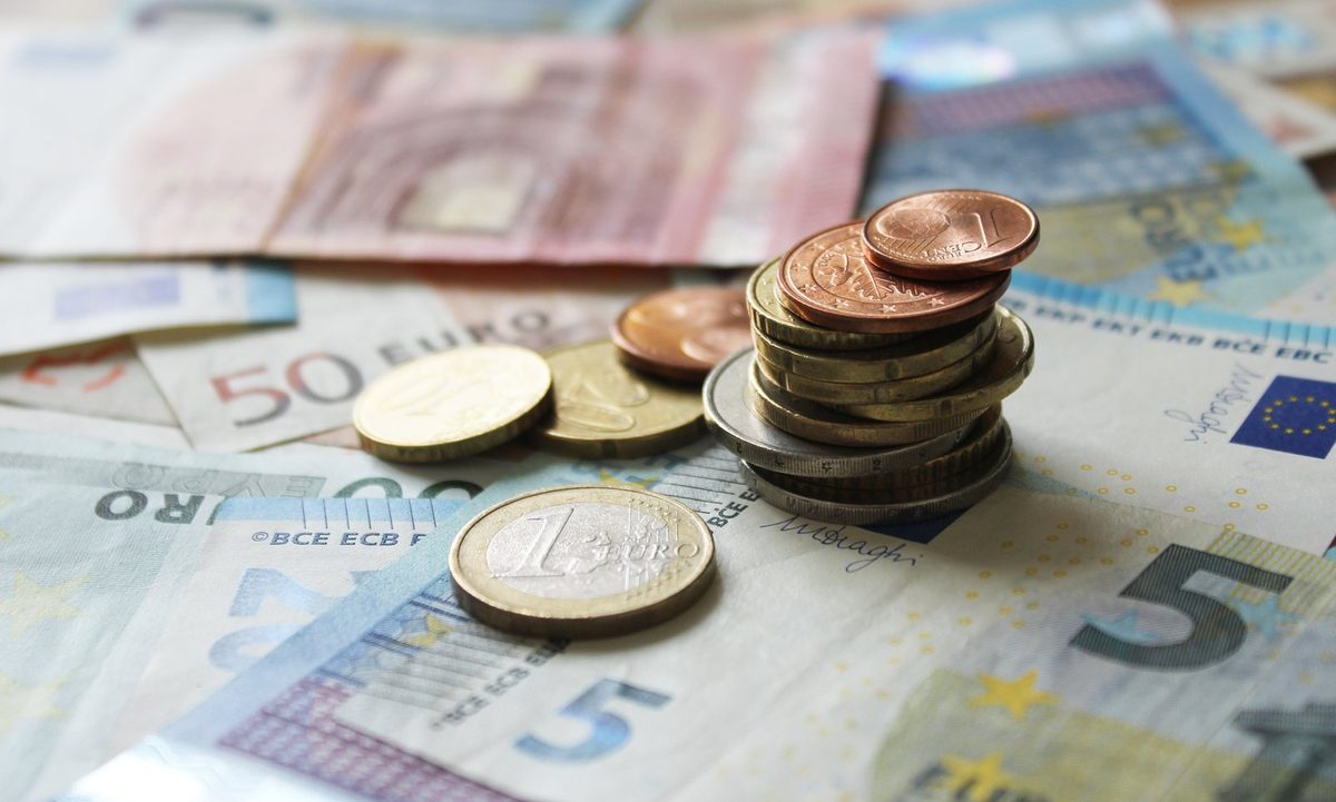Pareja joven sumando con una calculadora y documentos cuánto dinero necesita para comprar un piso, con las llaves de la vivienda sobre la mesa