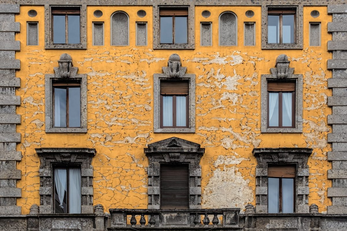 Facciata ocra di un palazzo residenziale vicino al Duomo di Milano, intonaco scrostato e finestre con persiane, immobile da rogitare