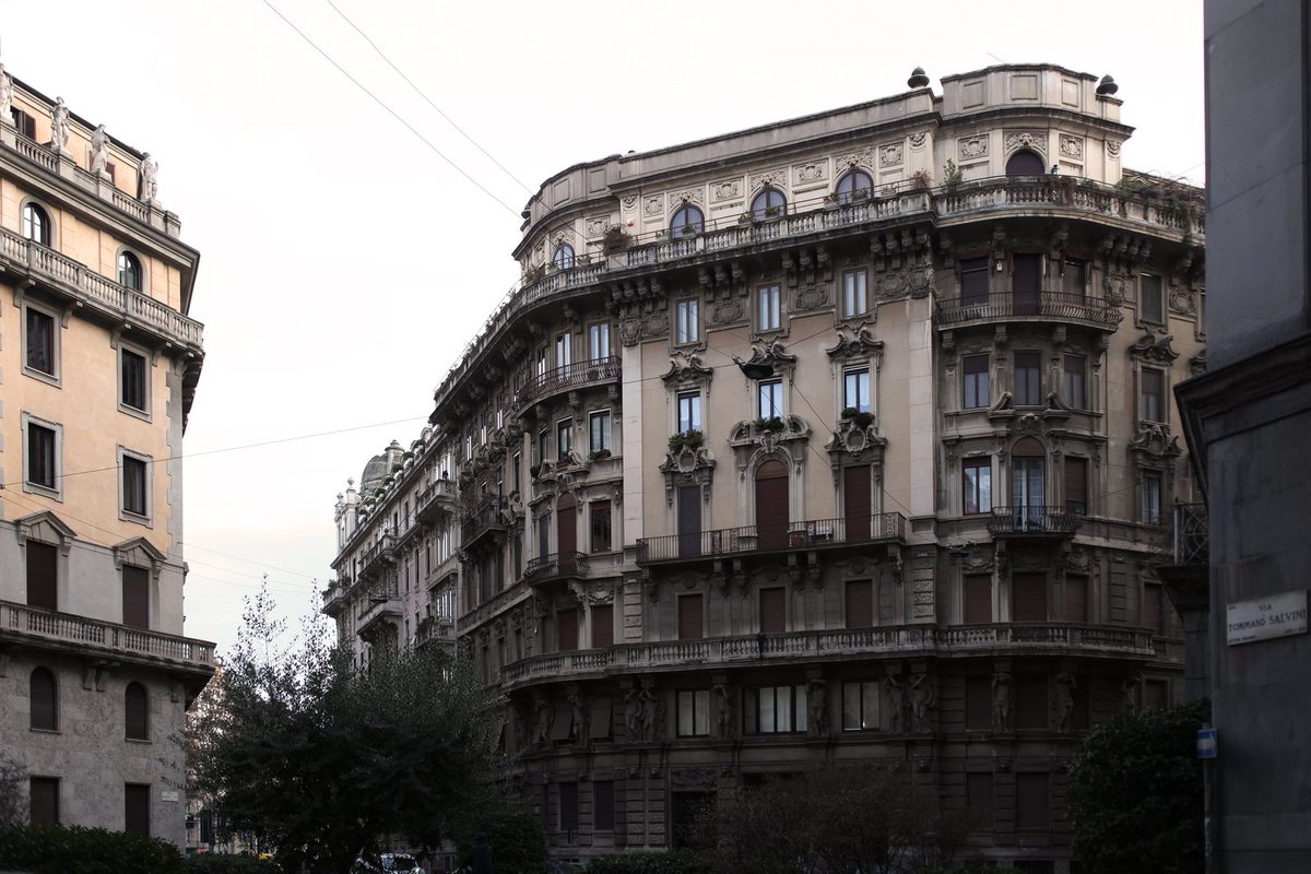 Facciate di palazzine residenziali in una città italiana, con un cartello Vendesi appeso a un balcone