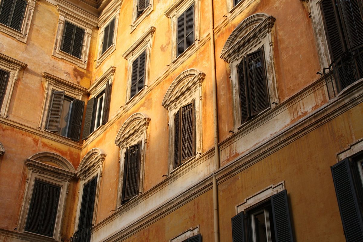 Giovane coppia con un taccuino davanti al portone di una palazzina italiana, mentre calcola la rata del mutuo prima di fare un'offerta